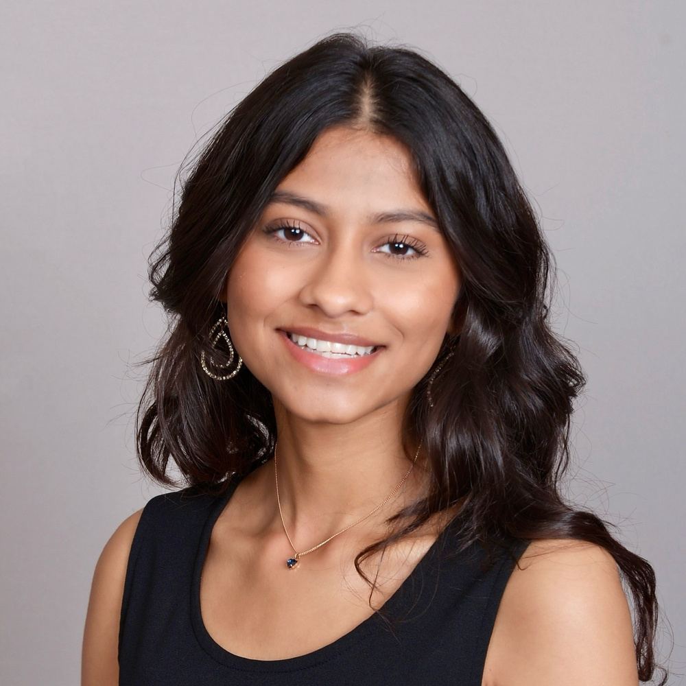 I am Divya Gupta. I am wearing a black dress in front of a flat gray background.