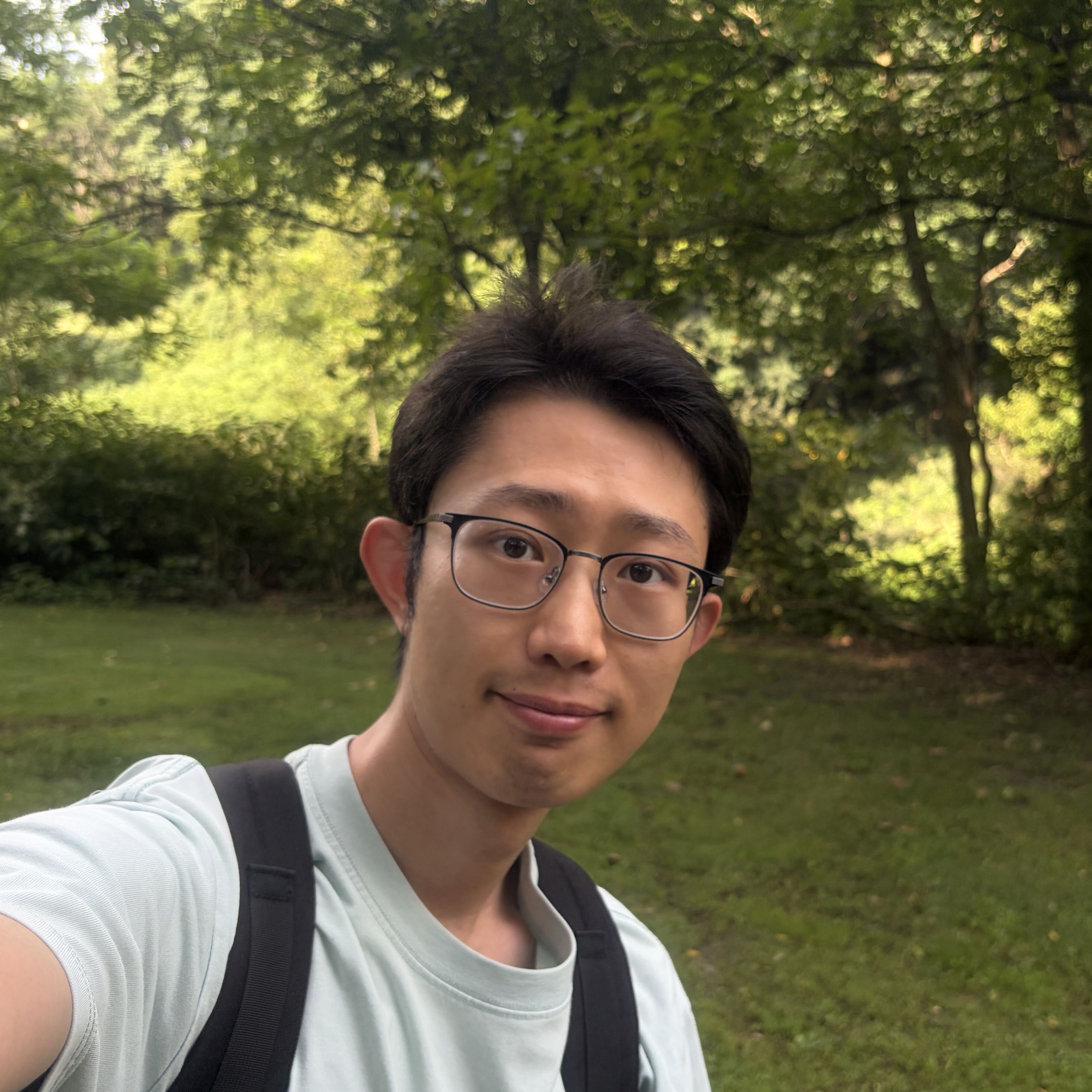I am Jinyu. I am wearing a light gren shirt and standing outside in front of trees.